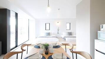 A modern, well-lit room with a dining table set for four, a bed with a view, and a small kitchen area.