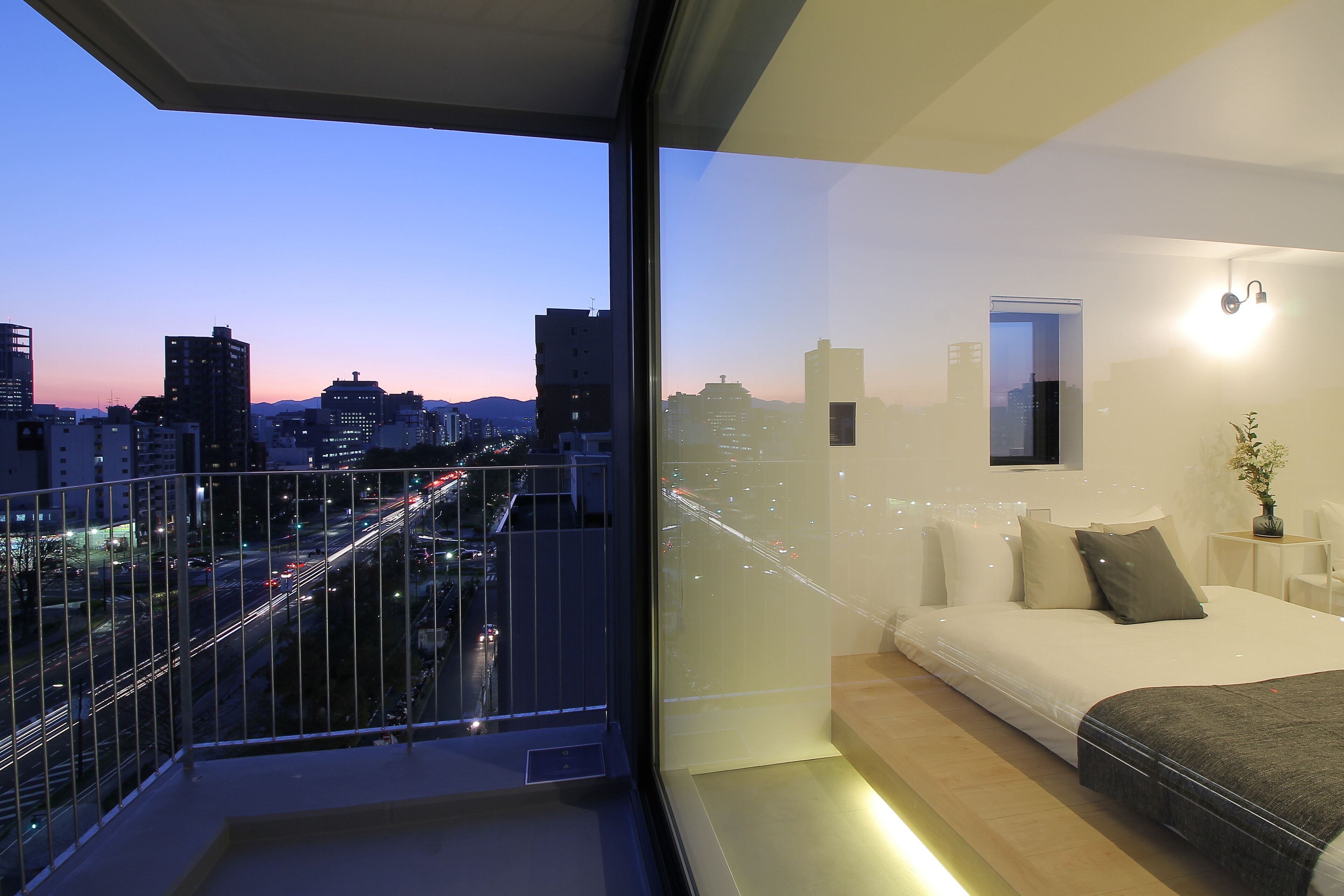A modern bedroom with a city view, a balcony, and a minimalist design.