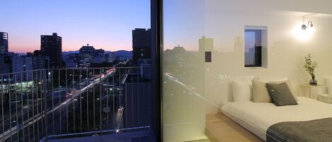 A modern bedroom with a city view, a balcony, and a minimalist design.