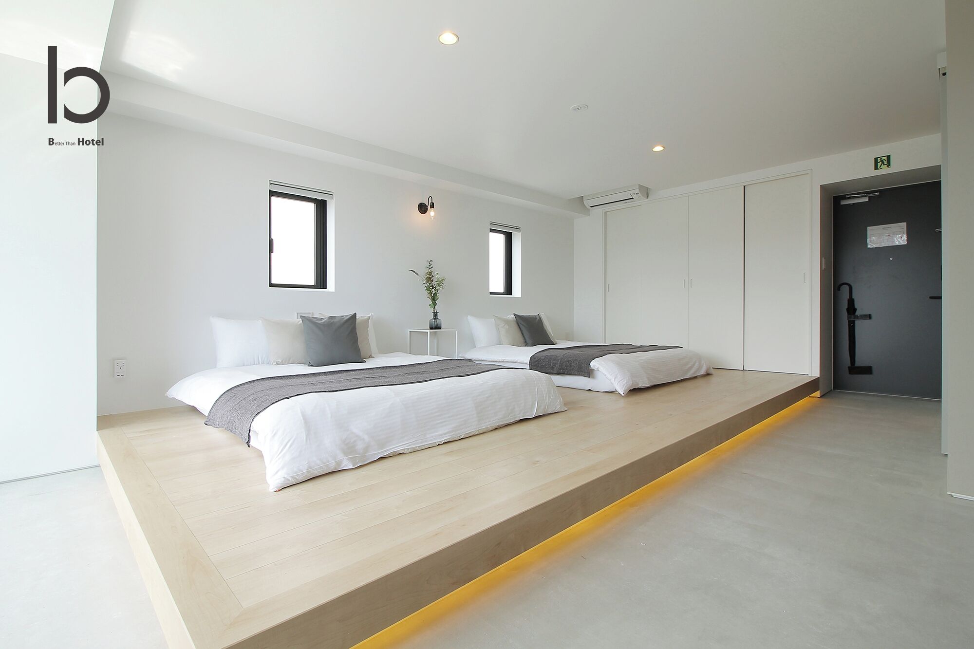 A modern hotel room with two beds, a small table with a plant, and a door to the bathroom.