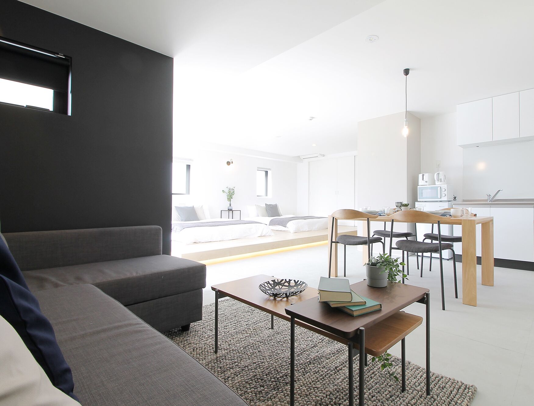 A modern living room with a sofa, a dining table with chairs, a kitchen area, and a view of the outside.