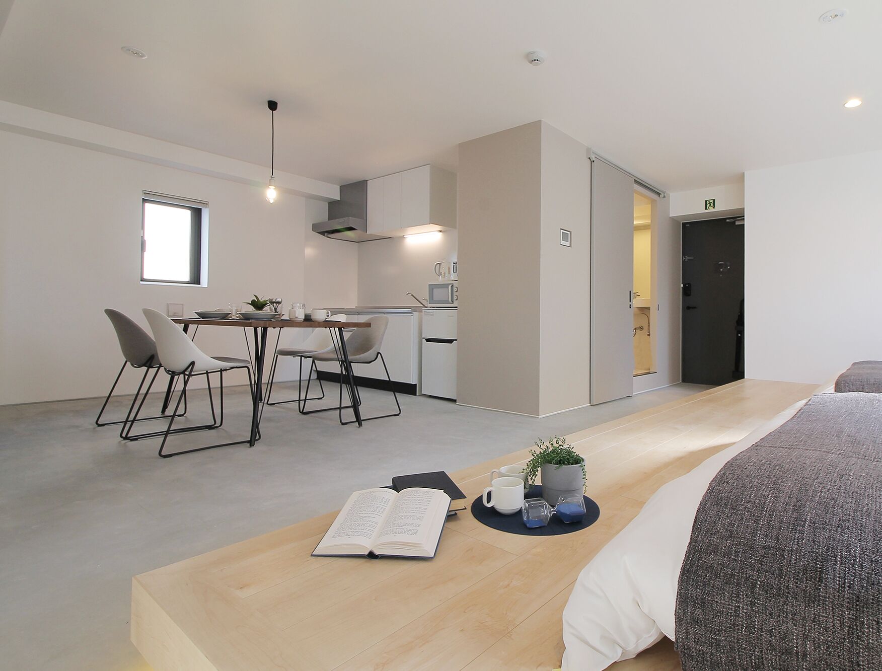 Quarto moderno com cama, área de refeições com cadeiras, cozinha e banheiro.