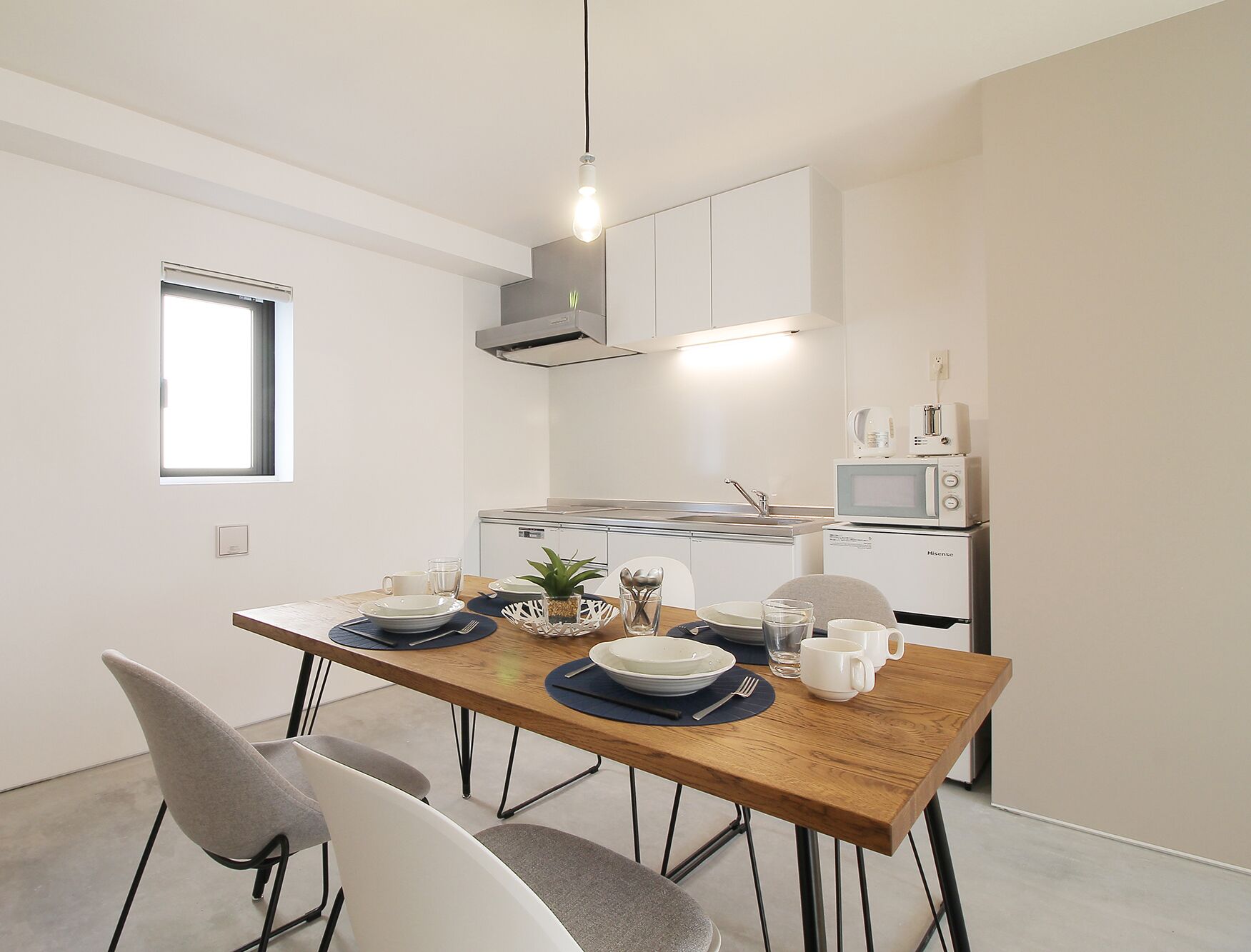 A modern kitchen with white cabinets, a microwave, and a sink. There is a dining table with plates, cups, and a plant.