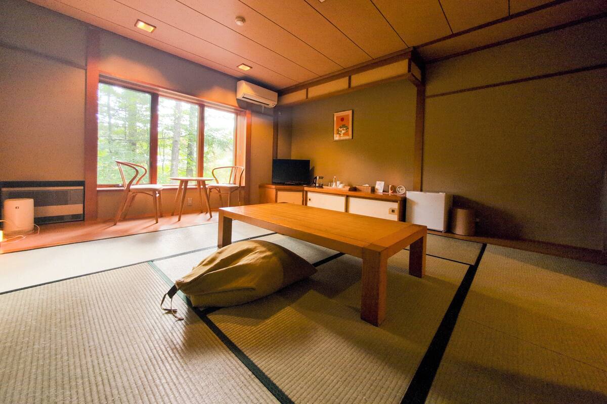 A traditional Japanese-style room with tatami flooring, a low table, a sofa, and a television.