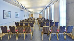A conference room with rows of chairs, a whiteboard, and framed artwork on the walls. - Ruth Daniel (Bat Yam)