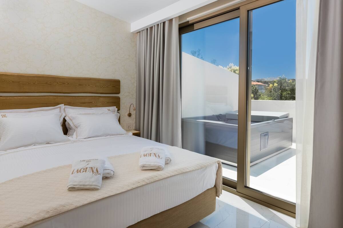Habitación de hotel moderna con una cama grande, un balcón con hidromasaje y una vista panorámica de la ciudad.