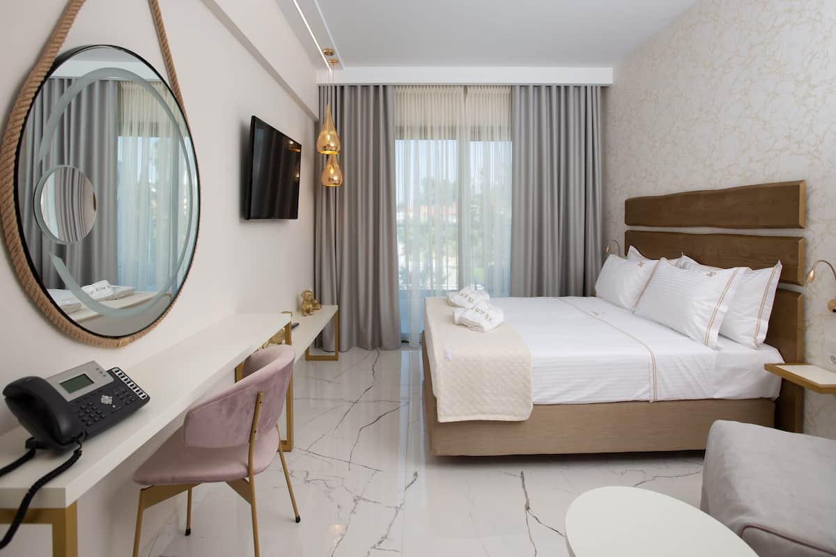 Habitación de hotel con cama, escritorio con teléfono, silla, televisión y un espejo grande.