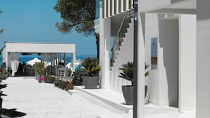 A white building with a covered outdoor area, potted plants, and a view of the sea. - Laguna Resort (Kassandra)