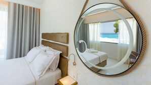 A hotel room with a bed, a bedside table, a round mirror, and a view of the sea through a window. - Laguna Resort (Kassandra)