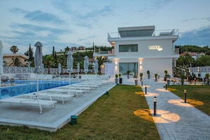 Un hôtel moderne doté d’une piscine, de chaises longues et d’un chemin éclairé.
