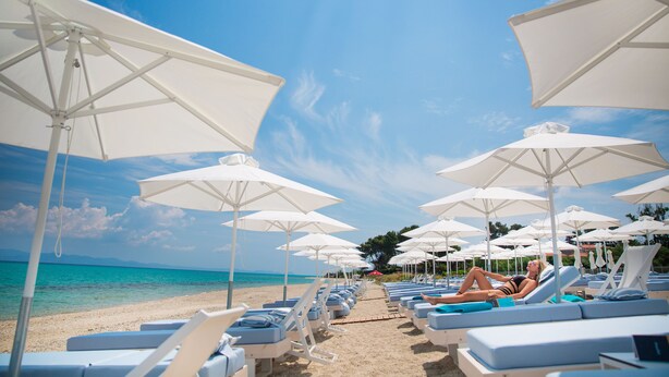 A beach with rows of sun loungers and umbrellas, a clear sky, and a calm sea. - Laguna Resort (Kassandra)