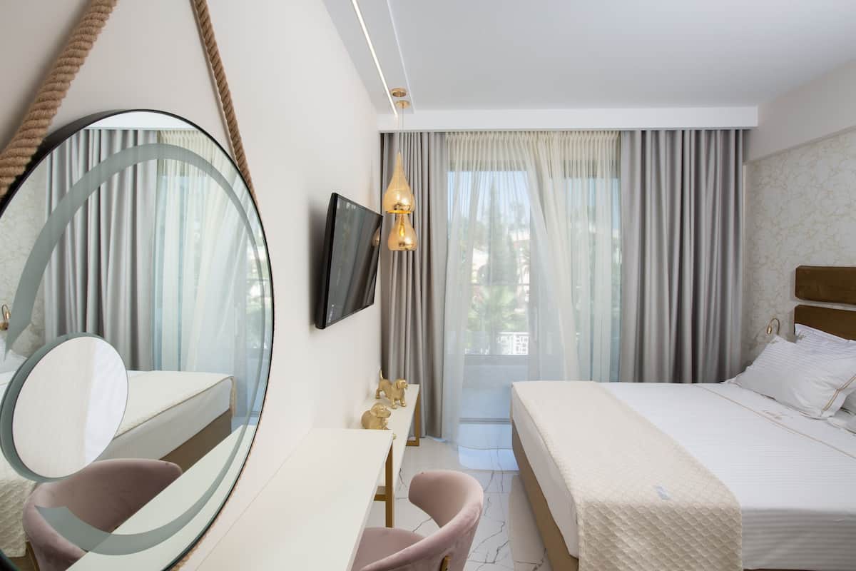 Una habitación de hotel con una cama, un escritorio con una silla, un televisor y un espejo grande.