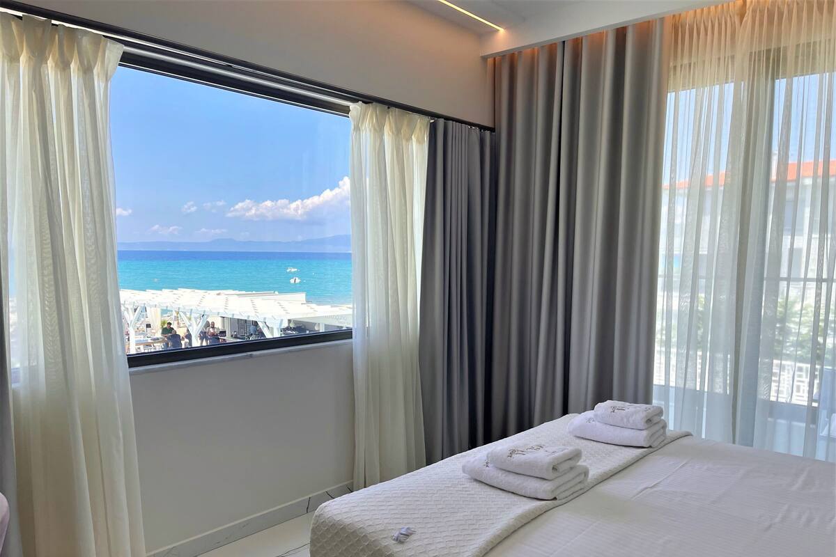 Una habitación de hotel con cama, vista a la playa y balcón con cortinas.