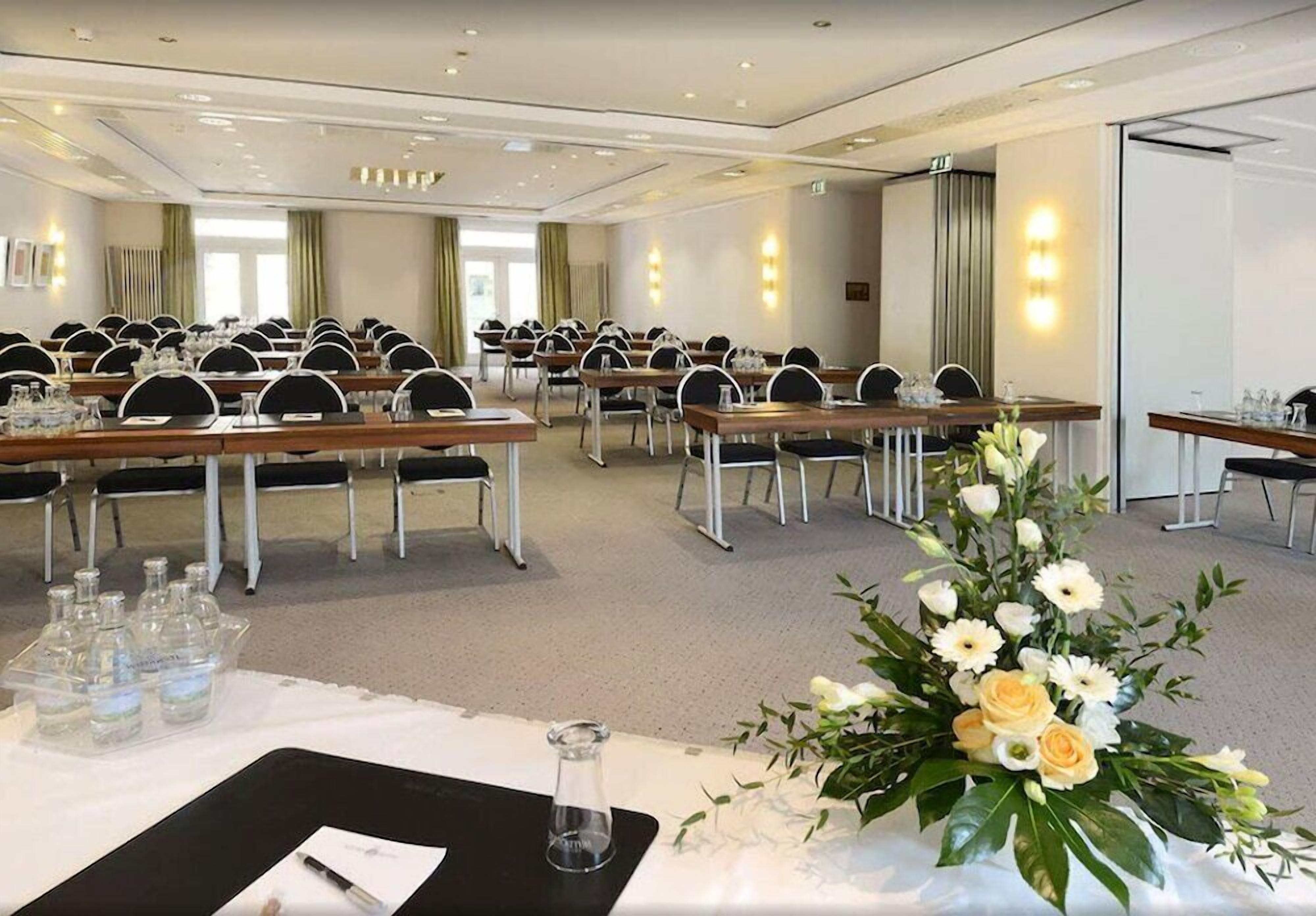 Ein Konferenzraum mit mehreren Tischen, Stühlen und einer floralen Tischdekoration.