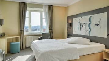 Ein Hotelzimmer mit einem großen Bett, einem Schreibtisch, einem Stuhl und einem Fenster mit Vorhängen.