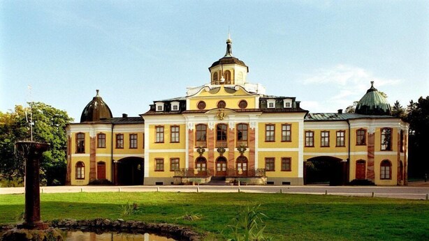 A large, yellow building with a central dome and two smaller domes on either side, surrounded by a well-maintained lawn and a small pond. - Kaiserin Augusta (Weimar)