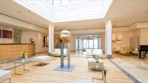 A spacious lobby with a high ceiling, a reception desk, seating areas, and a large spherical sculpture. - Kaiserin Augusta (Weimar)