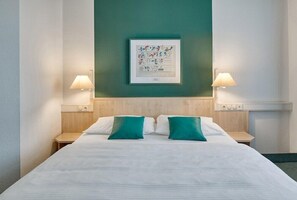 Habitación de hotel con una cama grande, dos mesitas de noche, una lámpara de pared e imagen enmarcada sobre la cama.