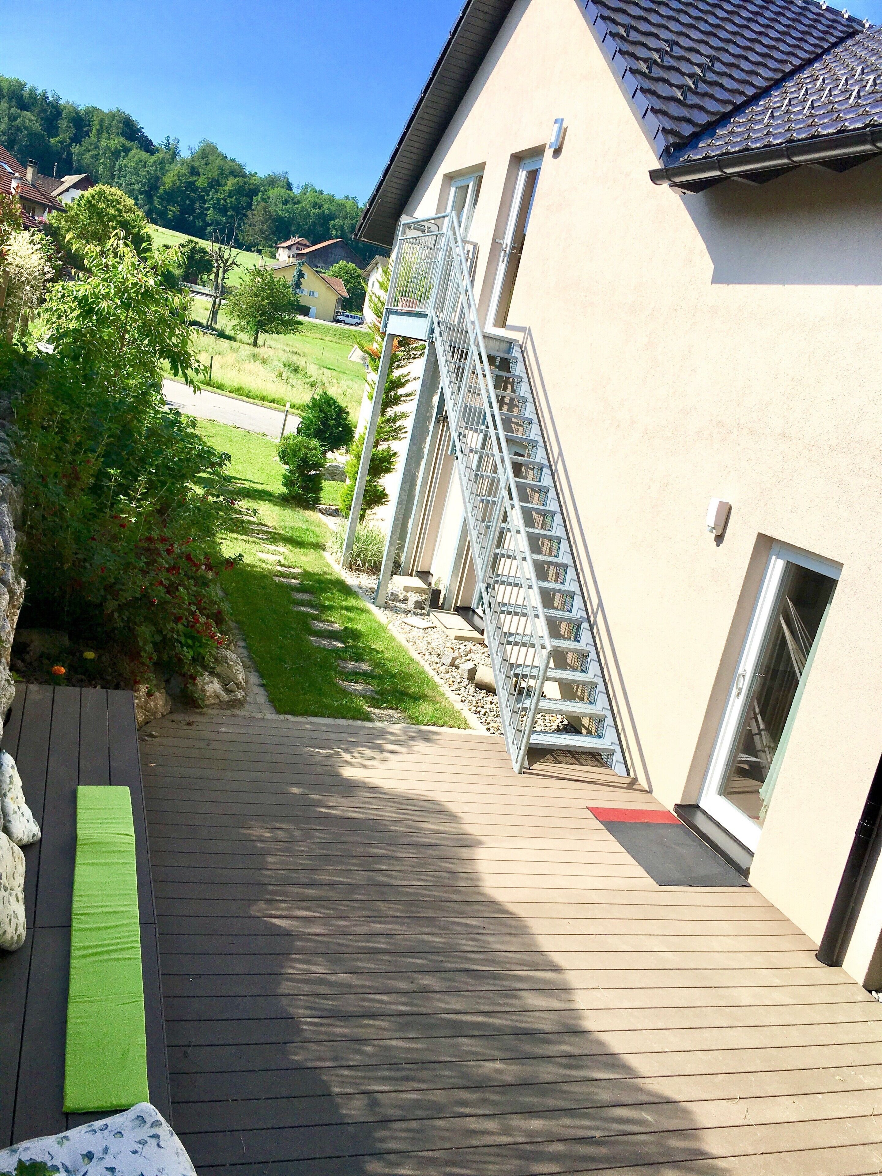 Eine Holzterrasse führt zu einem Gebäude mit einer Metalltreppe und einer Glastür.