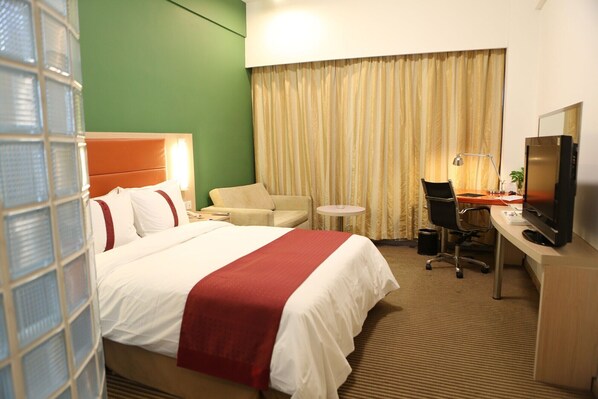 Una habitación de hotel con cama, escritorio con televisor, silla, una mesita y cortina.