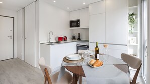 Une cuisine moderne avec des meubles blancs, un four à micro-ondes et un grille-pain rouge. On y trouve une table à manger dressée avec des assiettes, des verres et une bouteille de vin.