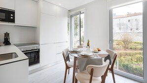 Une cuisine moderne avec des meubles blancs, un four encastré et une grande fenêtre donnant sur une cour.