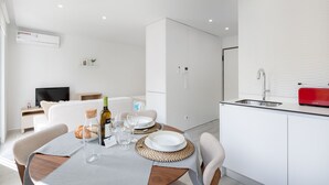 Une cuisine moderne avec des meubles blancs, un grille-pain rouge et un coin repas avec une table mise pour deux personnes.