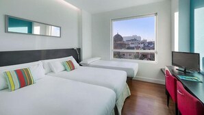 A hotel room with two beds, a desk with a TV, and a large window offering a city view. - Sea You Hotel Port Valencia (Valencia)