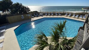 Una piscina con acqua cristallina, circondata da sdraio e una recinzione in legno, con vista sull'oceano.