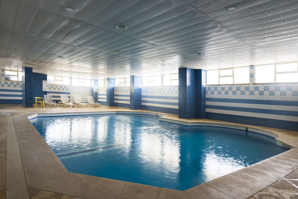 Una piscina interior con paredes de azulejos azules y blancos, un borde curvo y un techo con iluminación empotrada.