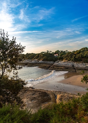Eine Küstenlandschaft mit Strand, felsigen Klippen und einem Haus auf einem Hügel.