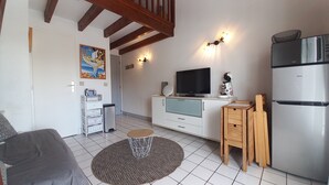Een knus woongedeelte met een kitchenette, een televisie, een koelkast en een schilderij aan de muur.