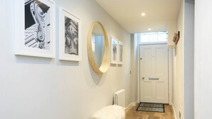 A hallway with a white door, a radiator, a white furry bench, and framed pictures on the wall. - JOIVY Vibrant City Centre 2-bed Apt. (Edinburgh)