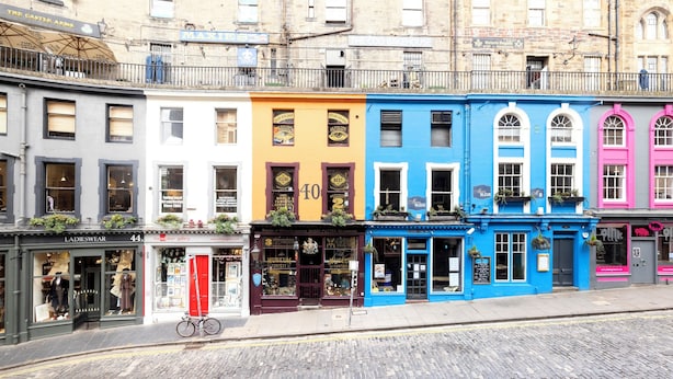 Una hilera de edificios coloridos con diferentes comercios, incluyendo una tienda de ropa de mujer y un museo.