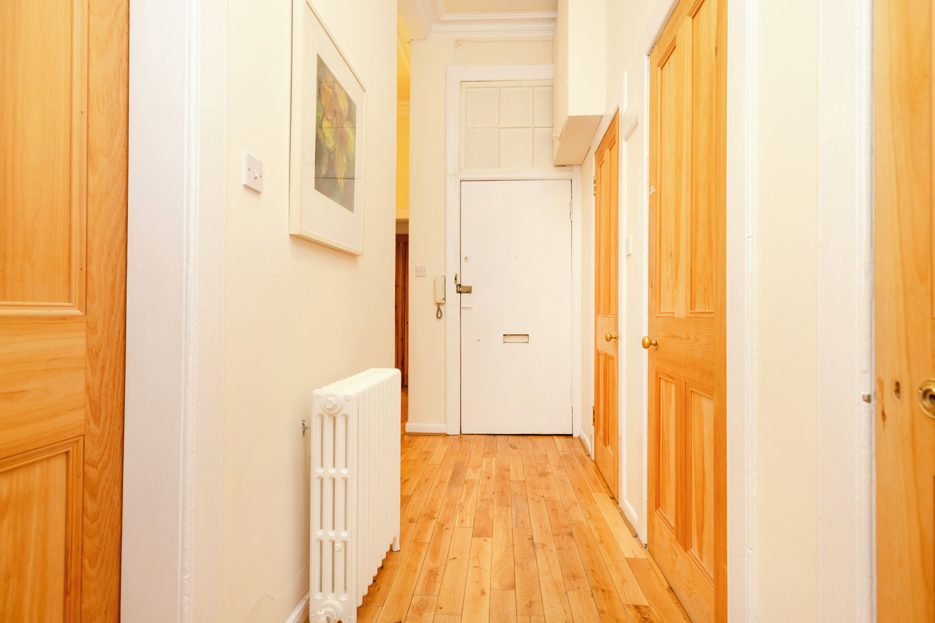 Un pasillo estrecho con puertas de madera y un radiador blanco.