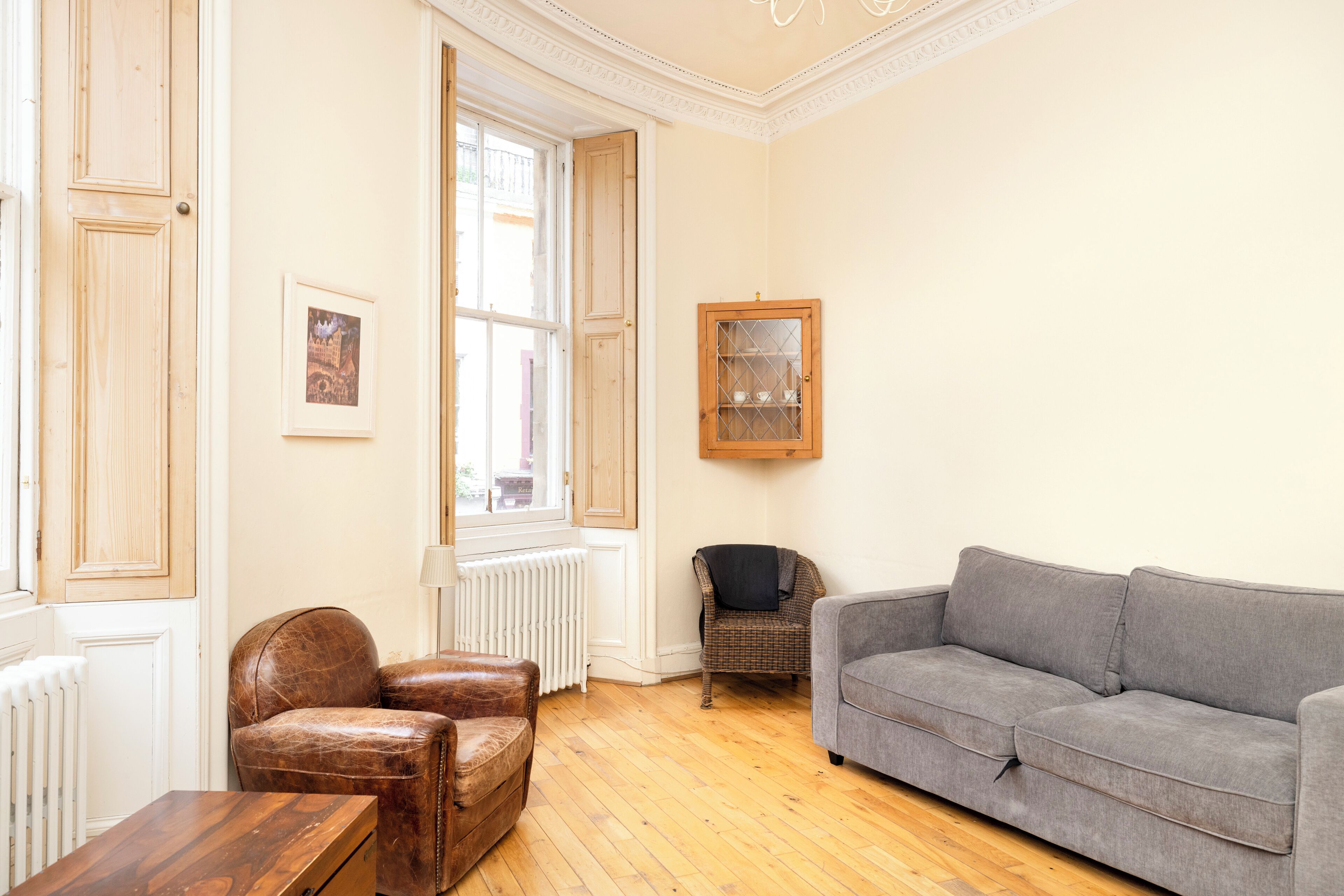 Un salon avec un plancher en bois, un canapé gris, un fauteuil en cuir marron, un meuble en bois et un tableau encadré accroché au mur.