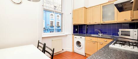 A compact kitchen with a washing machine, a microwave, and a window with a view of buildings.