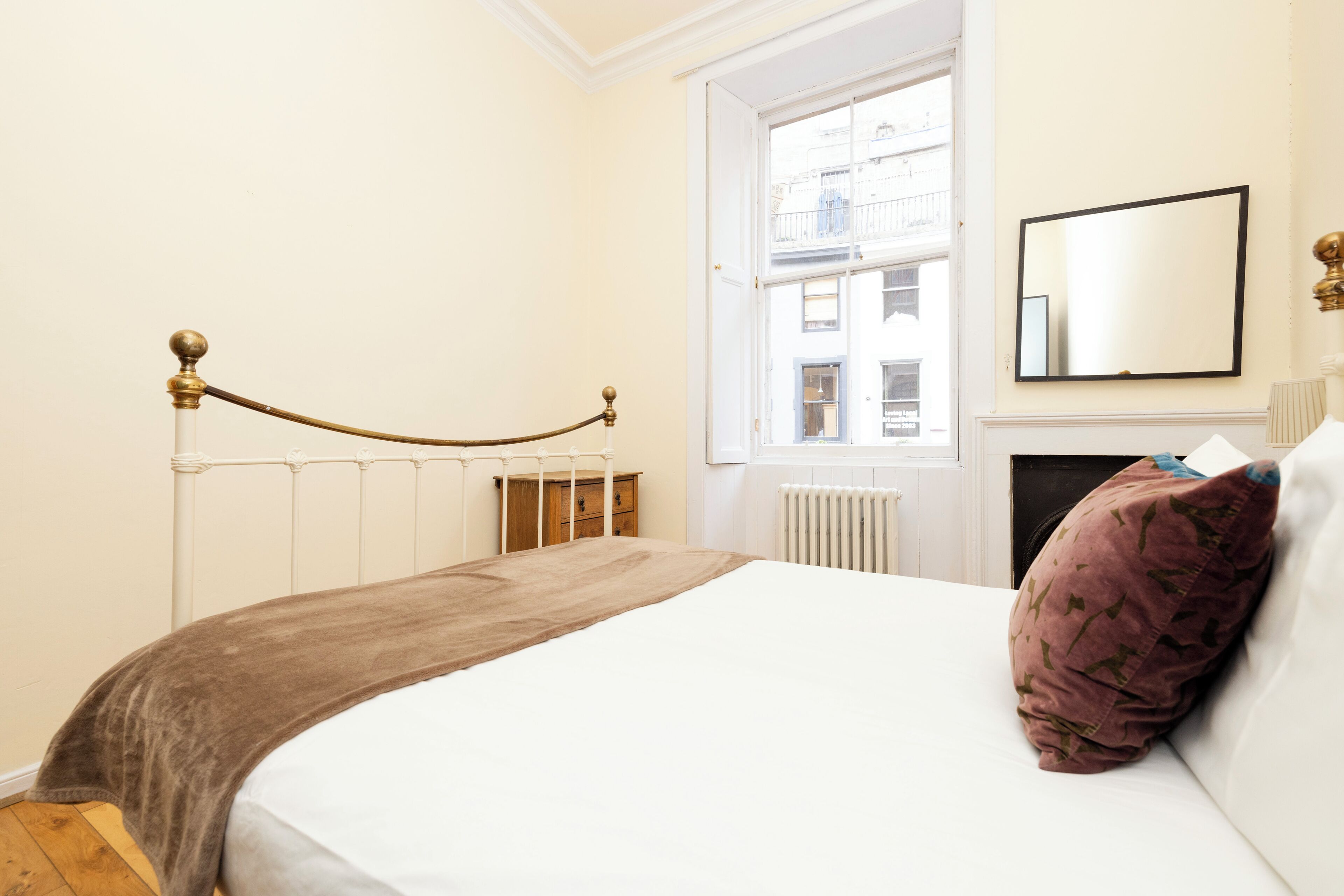 Een slaapkamer met een bed, een raam, een radiator en een spiegel aan de muur.