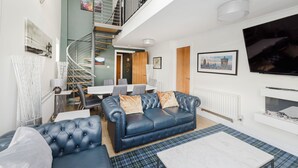 Ein modernes Wohnzimmer mit einem blauen Ledersofa, einem Esstisch und einer Treppe, die zu einer oberen Ebene führt.