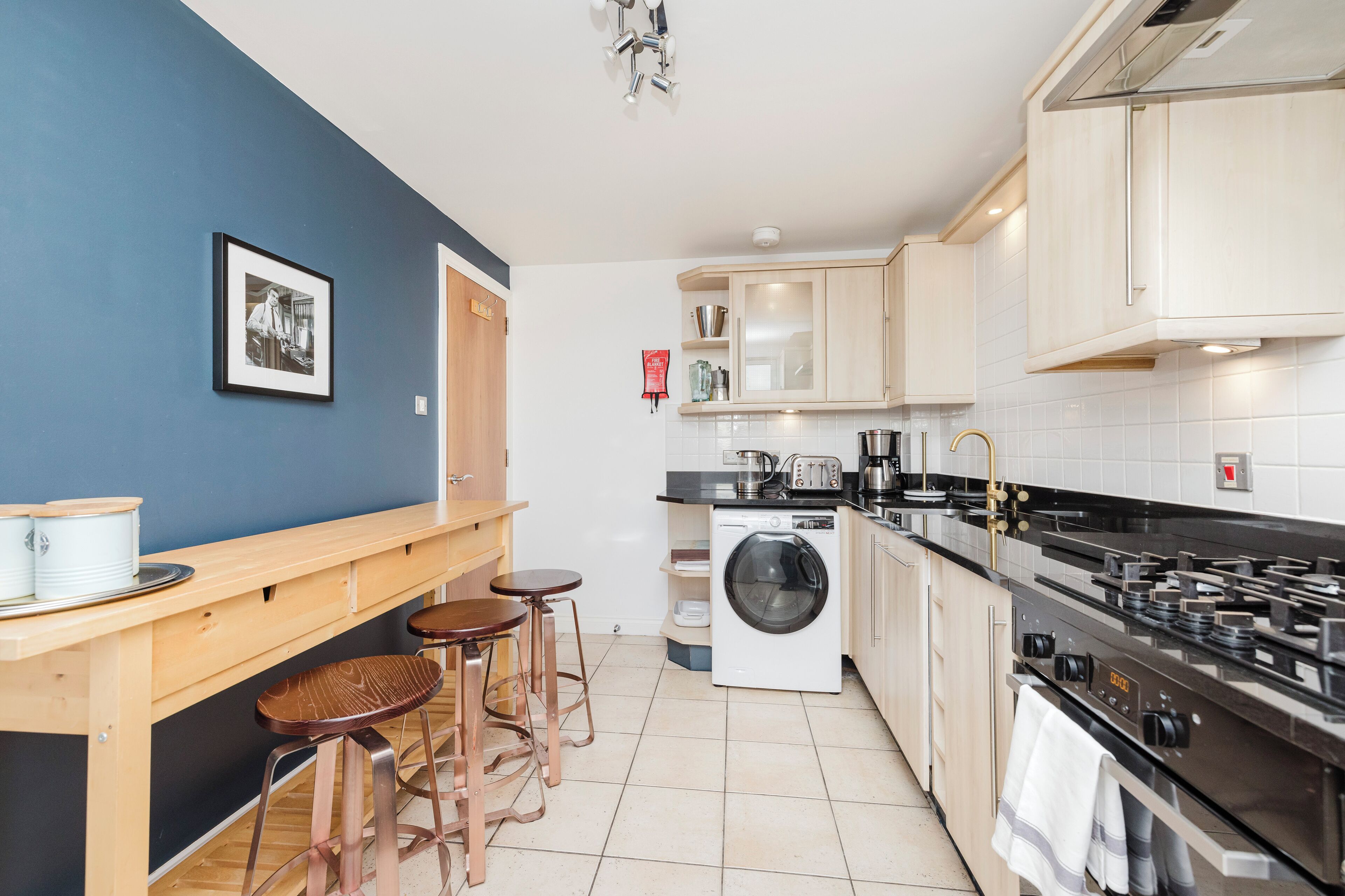 A compact kitchen with a washing machine, a stove, and a bar area with stools.