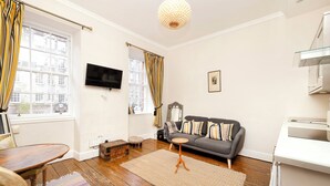 A living room with a wooden floor, a grey sofa, a small round table, and a TV mounted on the wall. - JOIVY Royal Mile Tower Apartment (Edinburgh)