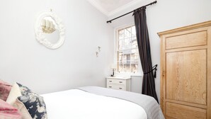 A bedroom with a bed, a dresser, a mirror, and a window with curtains. - JOIVY Royal Mile Tower Apartment (Edinburgh)