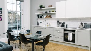 A modern kitchen with white cabinets, a dining area with a glass table and black chairs, and a view of the city through large windows.