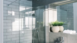 A modern bathroom with a glass-enclosed shower, a large mirror, and a potted plant.