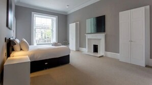A bedroom with a large bed, a fireplace, a wardrobe, and a TV on the wall.