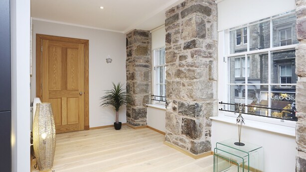 Una habitación amplia con puerta de madera, paredes de piedra, una planta en maceta y una mesa de cristal.