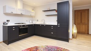 Una cocina moderna con armarios oscuros, encimeras blancas y un horno empotrado. Incluye una pequeña isla con un lavamanos y un jarrón decorativo.
