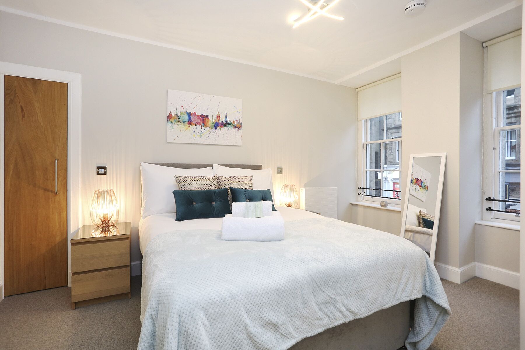 A bedroom with a bed, bedside tables, a mirror, and a window.