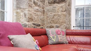 Un sofá de cuero rojo con almohadones decorativos frente a una pared de piedra.