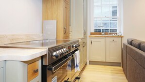 A modern kitchen with a built-in oven, a stainless steel range, and wooden cabinets. - JOIVY Newly Refurbished Apartment on the Historic Royal Mile (Edinburgh)
